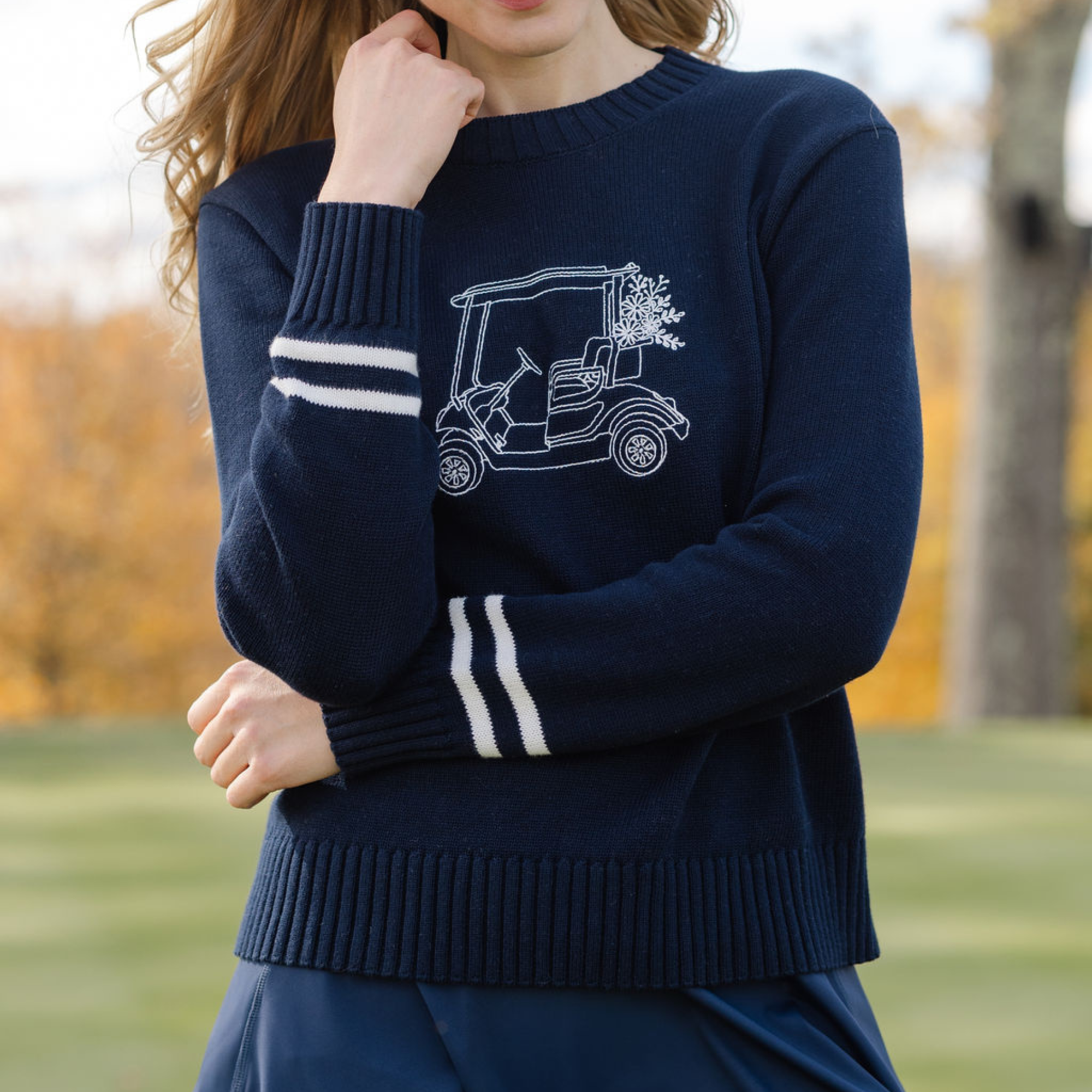 Person wearing a navy sweater with a white graphic of a golf cart on a blurred outdoor background