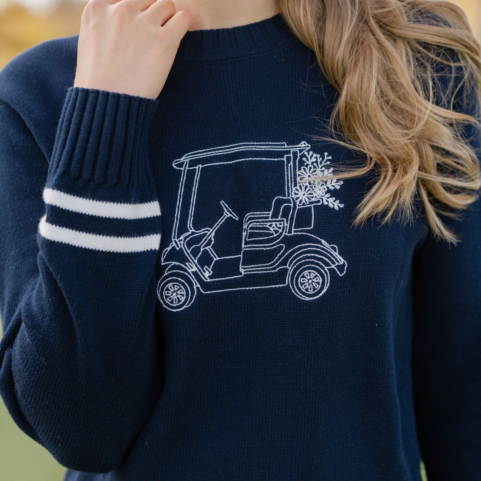 Navy blue sweater with a white golf cart design on a blurred background
