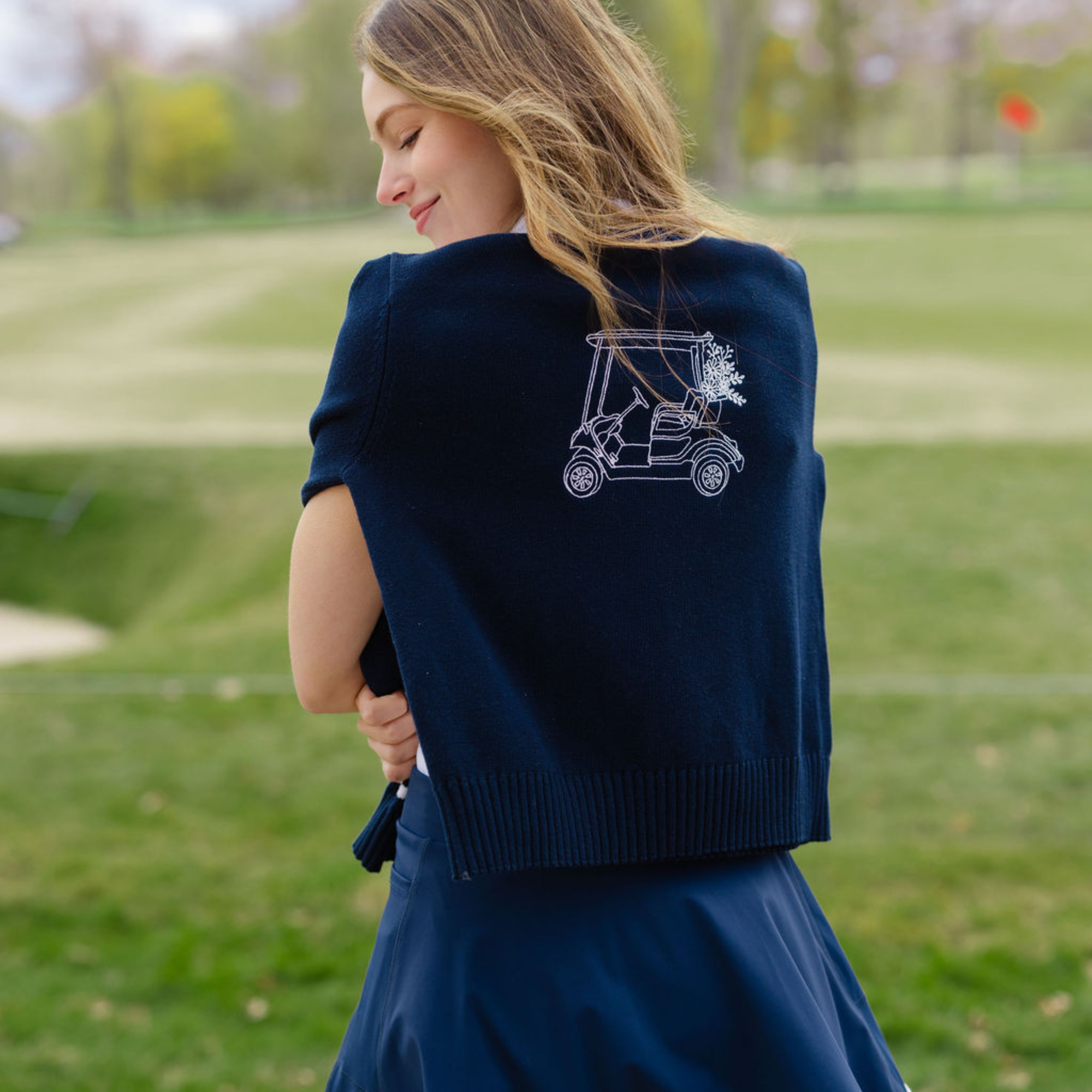 Woman wearing a navy blue cardigan with a golf cart design on a golf course