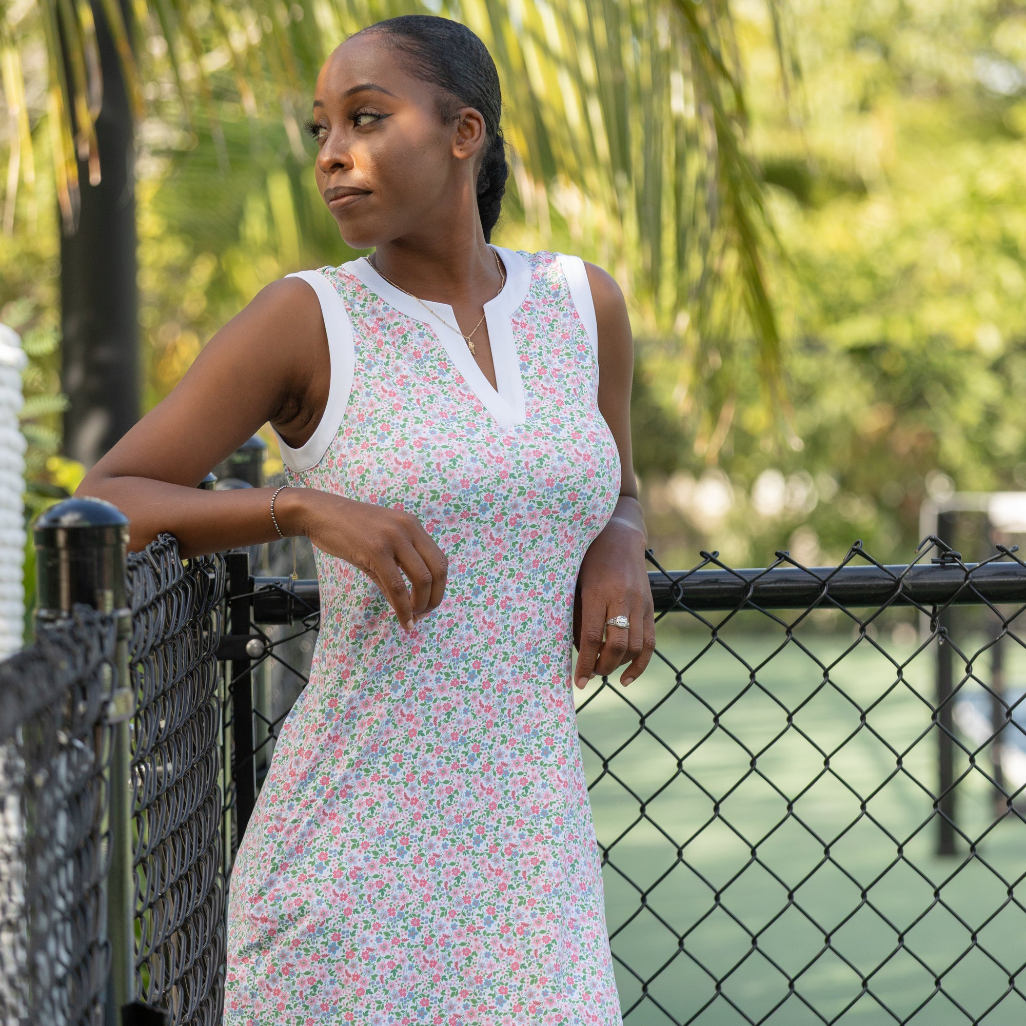 Woman in a floral dress standing by a fence with greenery in the background